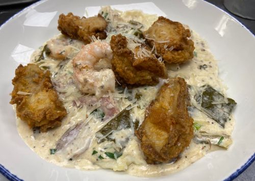 A creamy dish featuring fried shrimp and oysters on a bed of sauce with herbs and cheese.