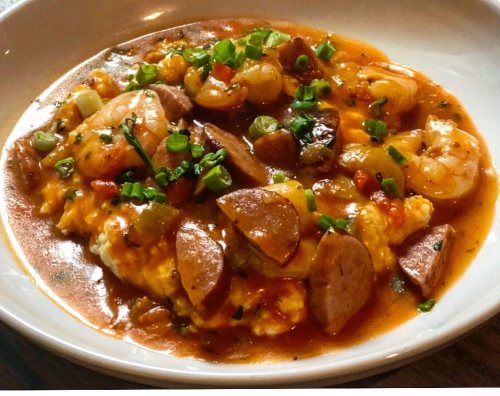 A bowl of shrimp and sausage stew served over creamy grits, garnished with chopped green onions.