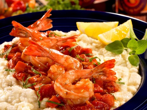 A vibrant dish of shrimp over creamy grits, topped with tomato sauce and garnished with lemon wedges and herbs.