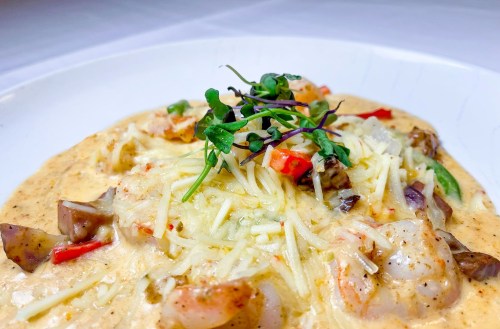 Creamy pasta dish with shrimp, vegetables, and cheese, garnished with microgreens on a white plate.