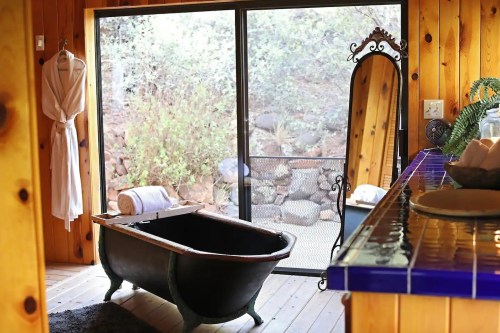 Cozy bathroom with a vintage bathtub, a mirror, and a view of nature through large glass doors.