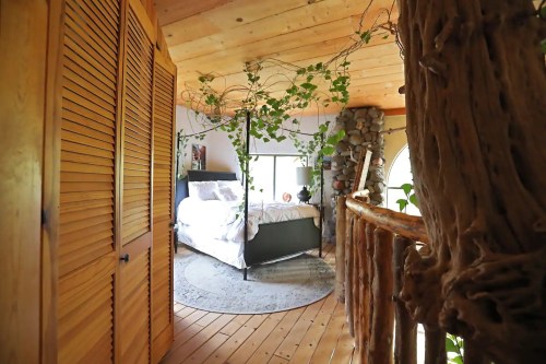 Cozy bedroom with wooden accents, a four-poster bed, and greenery, viewed from a rustic hallway.