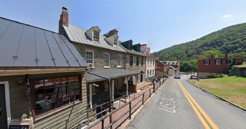 Historic buildings line a street with a mountain backdrop, featuring a mix of stone and wooden architecture.