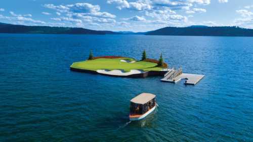 A boat approaches a golf green on a small island in a serene lake, surrounded by trees and blue skies.