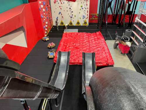 A view of a climbing gym featuring two slides, a red landing area, and climbing walls in the background.