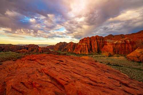 Vibrant red rock formations under a dramatic sky with clouds at sunset in a desert landscape.