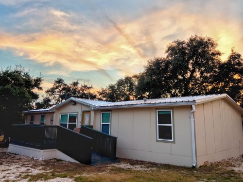 A single-story house with a ramp, surrounded by trees, under a colorful sunset sky.