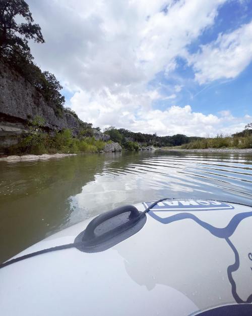 A view from a kayak on calm water, surrounded by rocky cliffs and lush greenery under a partly cloudy sky.