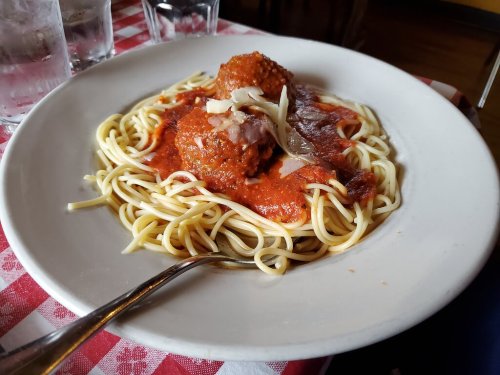 A plate of spaghetti topped with meatballs and marinara sauce, garnished with cheese, on a checkered tablecloth.
