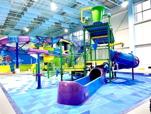 Colorful indoor water park with multiple slides and play structures, featuring purple and green designs.