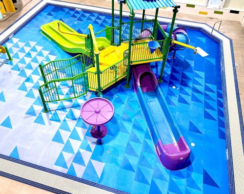 Colorful water play area featuring slides and splash features in a blue tiled pool.