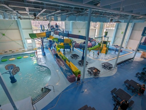 Indoor water park featuring slides, a pool, and seating areas, with people enjoying the attractions.