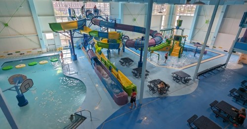 A vibrant indoor water park featuring slides, a pool, and seating areas, with people enjoying the attractions.