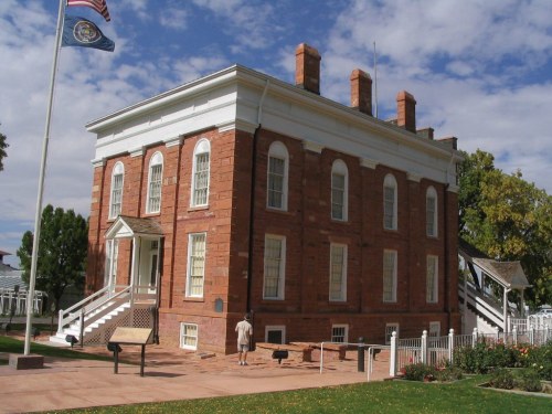 Historic red brick building with white trim, surrounded by greenery and a flagpole, under a blue sky with clouds.
