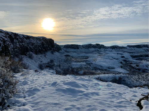 A snowy landscape with cliffs and valleys under a bright sun, casting a warm glow in a winter scene.