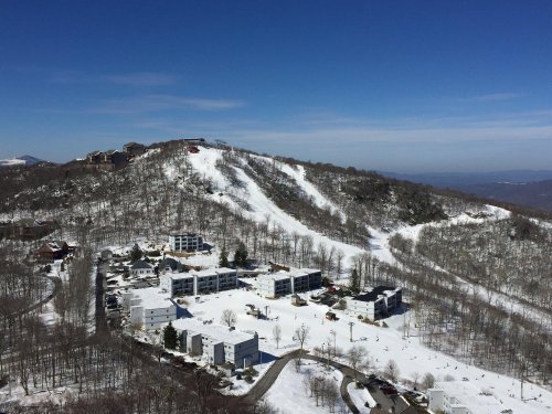 A snowy mountain landscape with ski slopes, residential buildings, and clear blue skies in the background.
