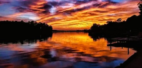 A vibrant sunset over a calm lake, with colorful clouds reflecting on the water's surface.