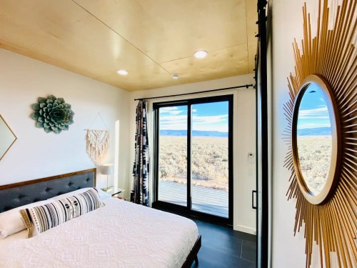 Bright bedroom with a large window overlooking a scenic landscape, featuring modern decor and a cozy bed.