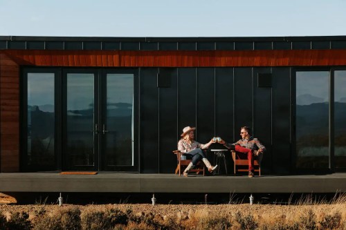 A couple enjoys drinks on a modern deck, surrounded by scenic views and mountains in the background.