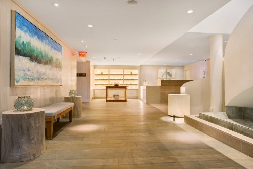 A modern, serene lobby with wooden accents, soft lighting, and a large abstract painting on the wall.