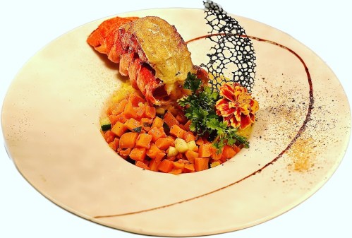 A gourmet dish featuring lobster, colorful vegetable medley, and decorative garnishes on an elegant plate.
