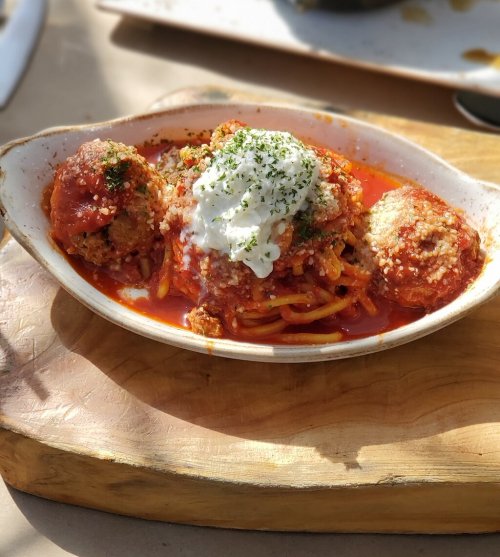 A bowl of spaghetti topped with meatballs, marinara sauce, and a dollop of sour cream, served on a wooden board.