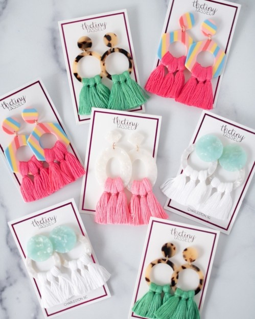 Colorful earrings displayed on cards, featuring tassels and various designs in pink, green, and neutral tones.