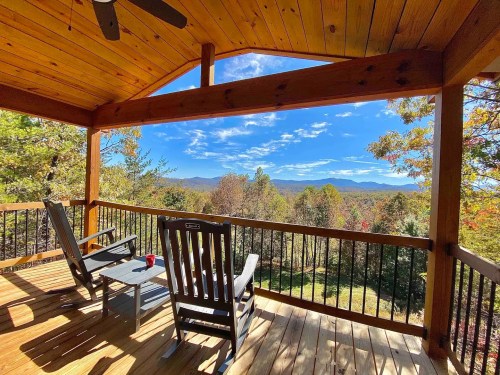 A cozy porch with two rocking chairs overlooking a scenic mountain view and colorful autumn trees.