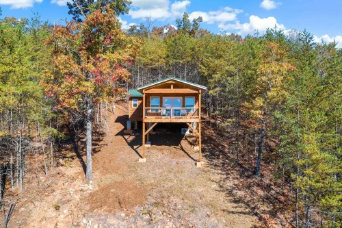 A wooden cabin on stilts surrounded by trees, with a clear blue sky and colorful autumn foliage.
