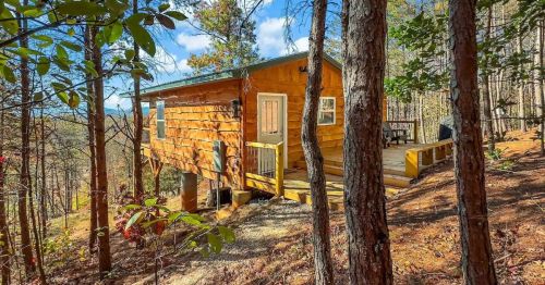 A cozy wooden cabin nestled among tall trees, with a deck overlooking a scenic landscape.