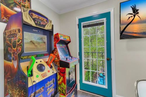 A cozy game room featuring arcade machines and a door leading to a scenic outdoor view.