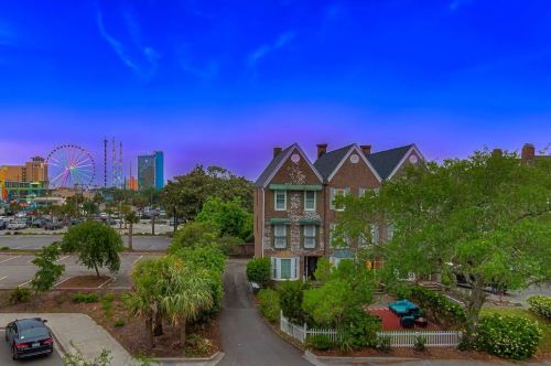 A charming brick house surrounded by greenery, with a colorful skyline and a ferris wheel in the background at dusk.