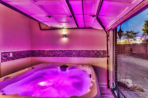 A cozy indoor hot tub with purple lighting, set in a garage-like space with a view of the outdoors.