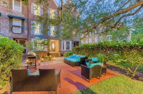 Cozy outdoor seating area with teal cushions, surrounded by greenery and brick buildings at dusk.