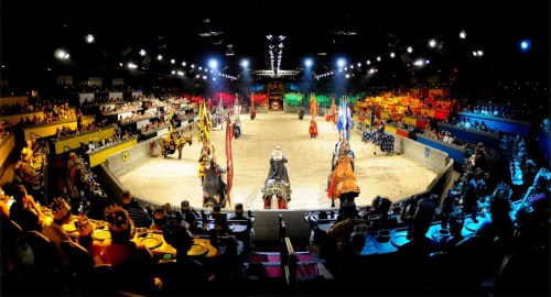 A vibrant medieval-themed arena with knights, colorful banners, and an audience watching a jousting event.