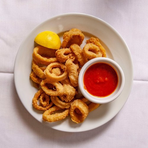 A plate of crispy fried calamari rings with a lemon wedge and marinara sauce for dipping.