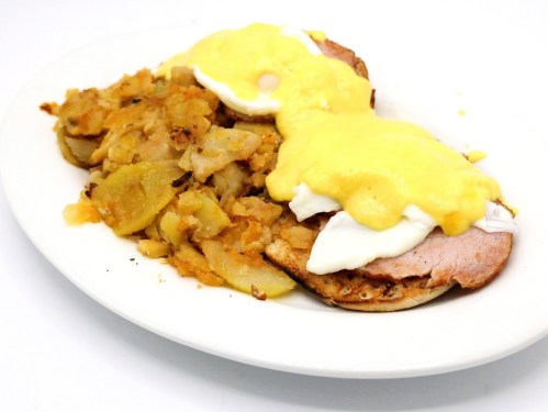 A plate of eggs Benedict with poached eggs and hollandaise sauce, served with a side of seasoned hash browns.