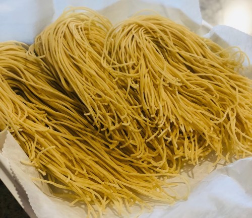 A close-up of uncooked spaghetti noodles arranged in a pile on a white paper towel.