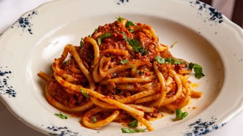 A plate of pasta with a rich meat sauce, garnished with fresh herbs.