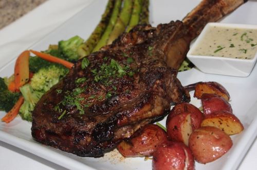 A beautifully plated meal featuring a large ribeye steak, roasted potatoes, asparagus, broccoli, and a creamy sauce.