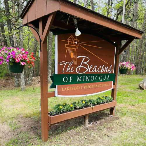 Sign for "The Beacons of Minocqua" Lakefront Resort and Suites, surrounded by flowers and trees.