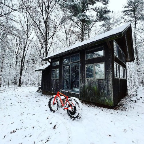 A red fat bike parked in front of a modern cabin surrounded by snow-covered trees.