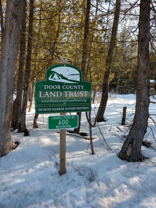 Sign for Door County Land Trust at Detroit Harbor Nature Preserve, surrounded by snow and trees.