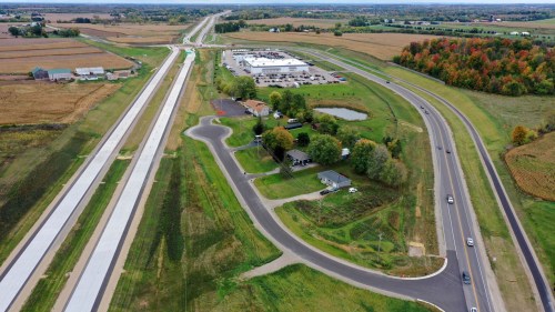Aerial view of a highway intersection with a commercial building, fields, and a small pond nearby.