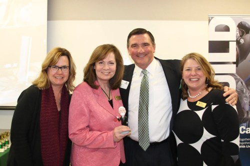 Four smiling individuals pose together, one holding a small figurine, at a celebratory event.