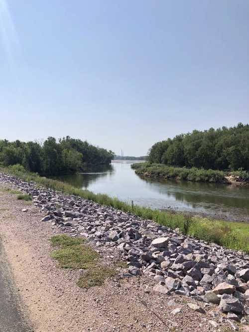 A serene river scene bordered by greenery and rocky banks under a clear blue sky.