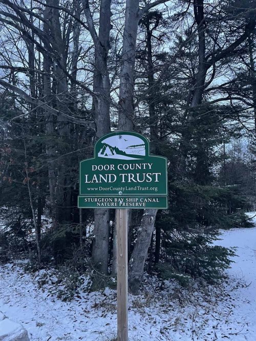 Sign for Door County Land Trust at Sturgeon Bay Ship Canal Nature Preserve, surrounded by trees and snow.