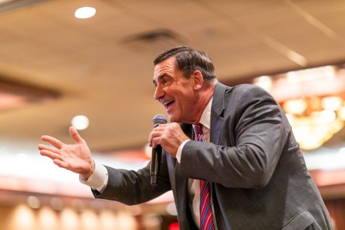 A man in a suit passionately speaks into a microphone, gesturing with his hand in a lively setting.