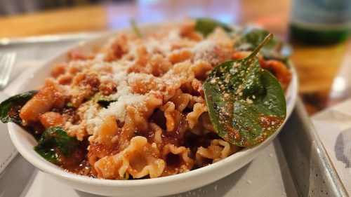 A bowl of pasta with spinach, topped with cheese and a rich tomato sauce, served on a tray.