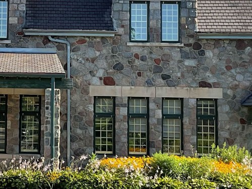 A stone house with green windows and a flower garden in front, featuring vibrant yellow and green plants.